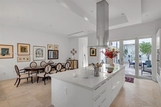 kitchen with cooktop, a kitchen island, island exhaust hood, a raised ceiling, and white cabinetry