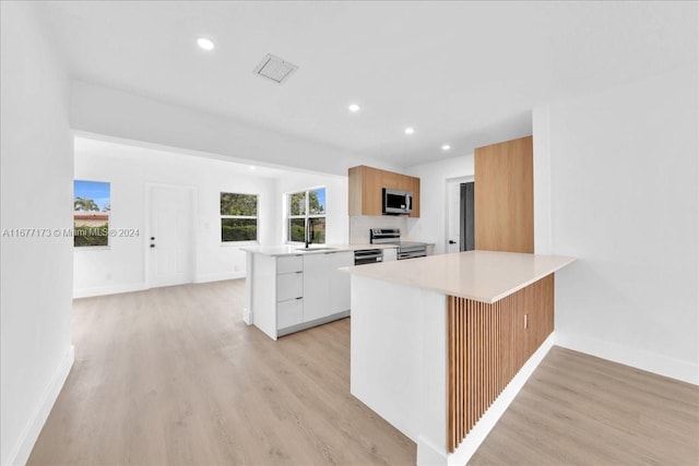 kitchen featuring kitchen peninsula, stainless steel appliances, white cabinetry, and light hardwood / wood-style floors