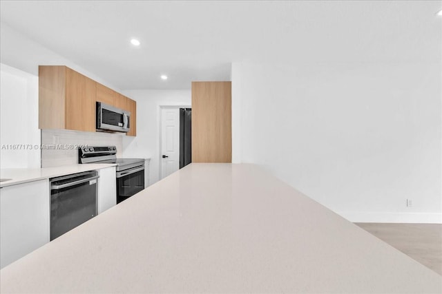 kitchen with decorative backsplash, stainless steel appliances, and light hardwood / wood-style floors