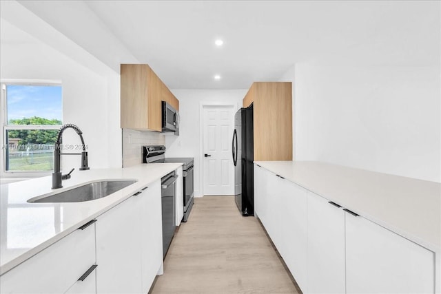 kitchen featuring white cabinets, black appliances, light wood-type flooring, and sink