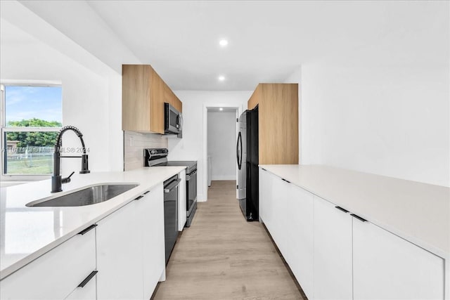 kitchen featuring decorative backsplash, black appliances, sink, white cabinets, and light hardwood / wood-style floors