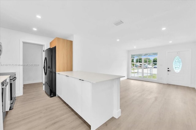 kitchen featuring white cabinetry, black refrigerator, stainless steel range with electric cooktop, and light hardwood / wood-style floors