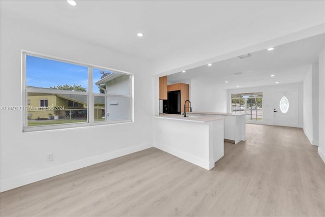 kitchen with kitchen peninsula, black refrigerator, sink, white cabinets, and light hardwood / wood-style floors