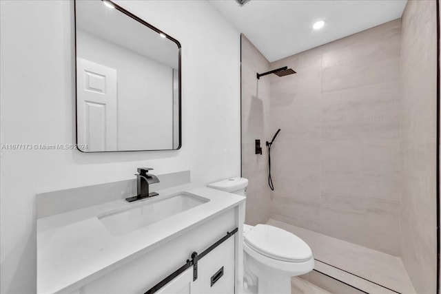 bathroom featuring a tile shower, vanity, and toilet