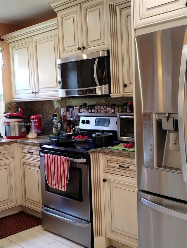 kitchen with backsplash, dark stone countertops, stainless steel appliances, and cream cabinets