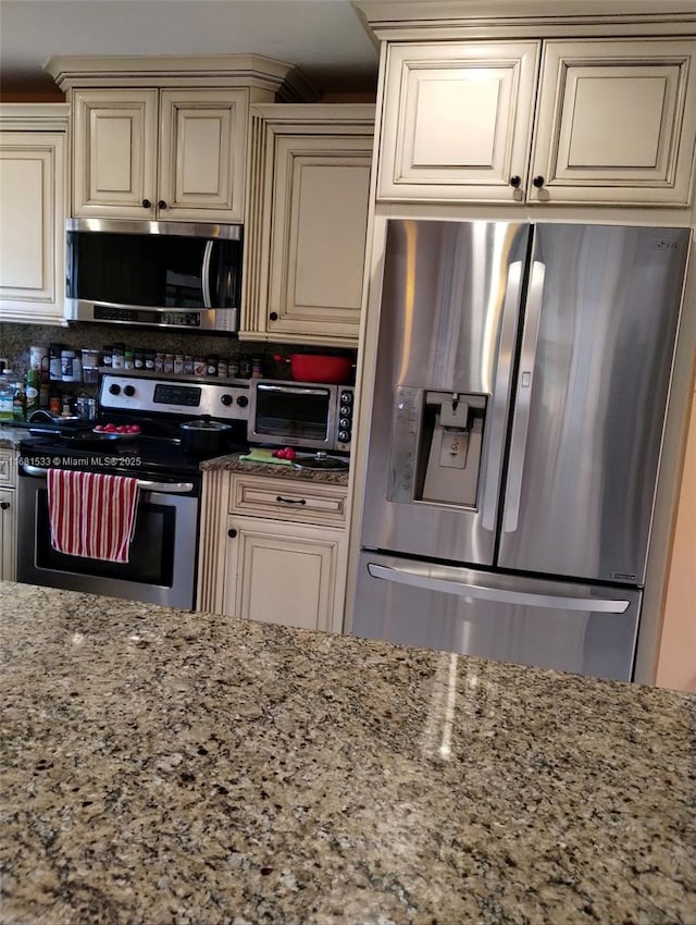 kitchen featuring appliances with stainless steel finishes, cream cabinetry, and light stone counters