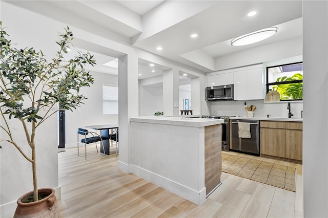 kitchen with white cabinetry, sink, stainless steel appliances, kitchen peninsula, and light wood-type flooring