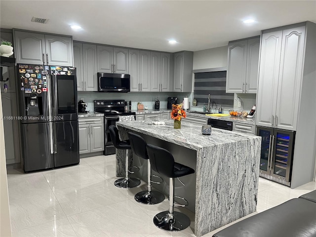 kitchen featuring beverage cooler, light stone countertops, stainless steel appliances, gray cabinetry, and a center island