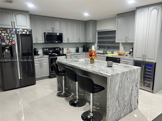 kitchen featuring a kitchen island, a breakfast bar area, stainless steel appliances, light stone countertops, and beverage cooler