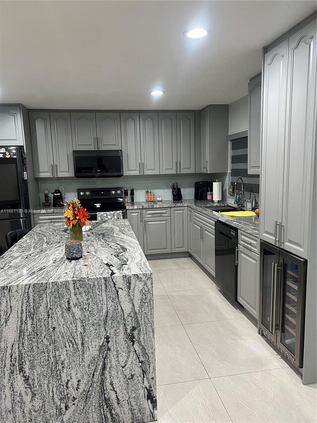 kitchen featuring light stone countertops, black appliances, sink, and gray cabinetry