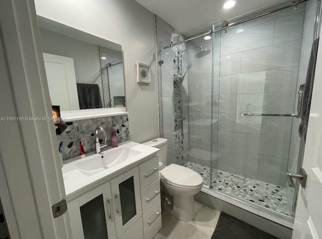 bathroom with vanity, toilet, a shower with shower door, and backsplash