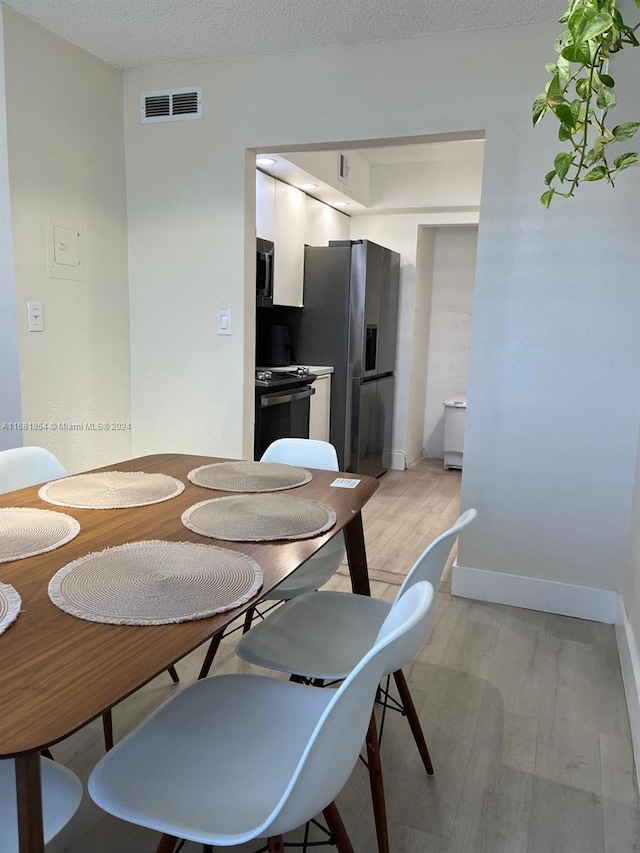 dining room with a textured ceiling and light hardwood / wood-style flooring