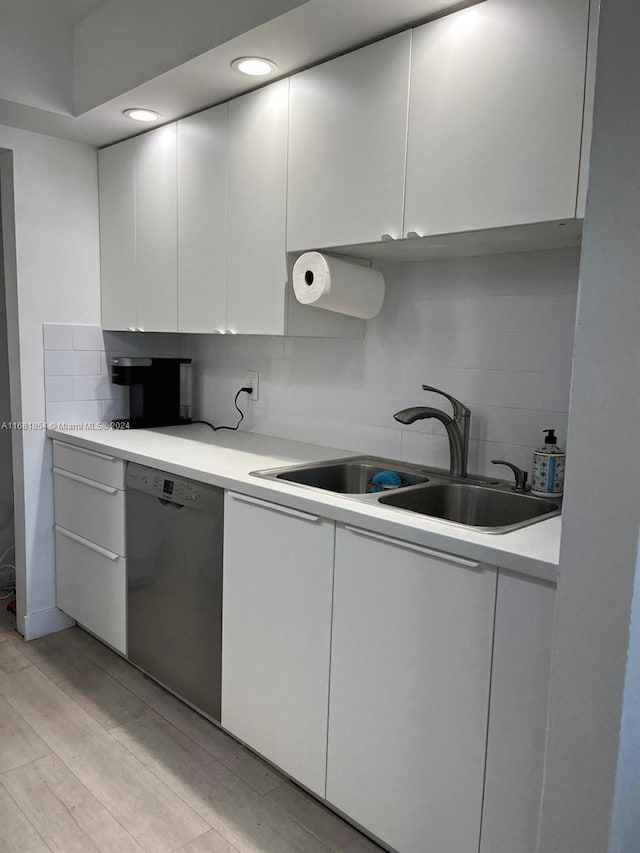 kitchen featuring backsplash, white cabinetry, stainless steel dishwasher, light wood-type flooring, and sink