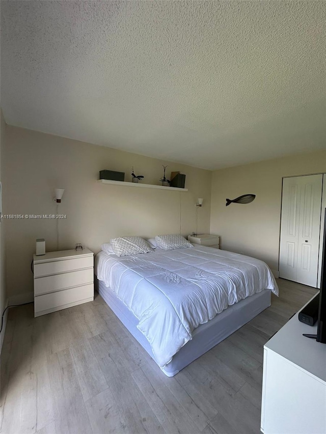 bedroom with a closet, a textured ceiling, and light wood-type flooring