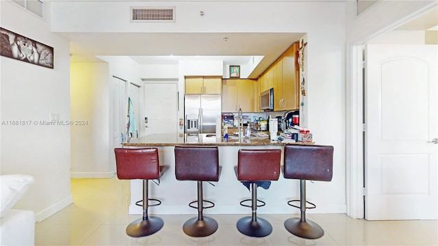 kitchen with a kitchen bar, kitchen peninsula, light tile patterned flooring, and stainless steel appliances