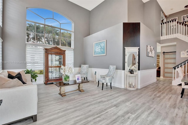 living room with a towering ceiling, light hardwood / wood-style flooring, and a barn door