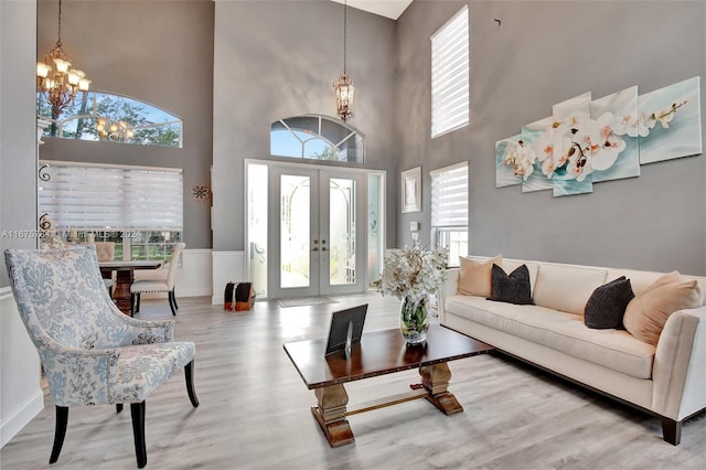 living room featuring french doors, a notable chandelier, wood-type flooring, and a high ceiling