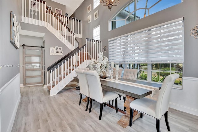 dining space featuring a towering ceiling, a healthy amount of sunlight, a barn door, and hardwood / wood-style flooring