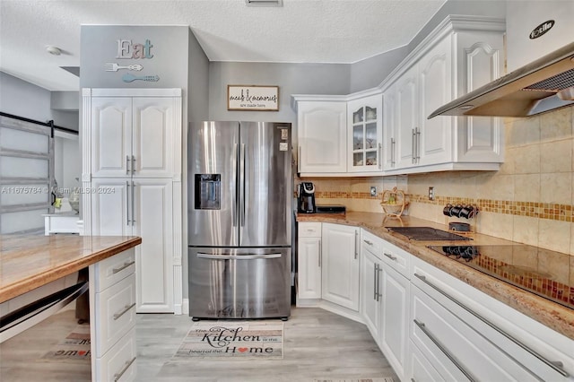 kitchen with wall chimney exhaust hood, stainless steel fridge, a barn door, white cabinets, and light hardwood / wood-style floors