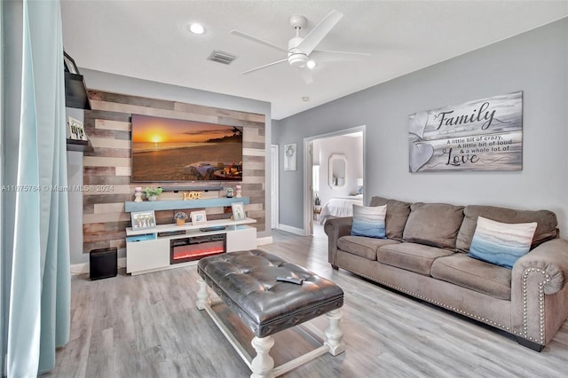 living room with ceiling fan, light wood-type flooring, and wooden walls