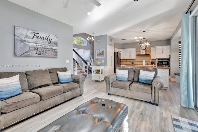 living room with a textured ceiling, ceiling fan with notable chandelier, and light wood-type flooring