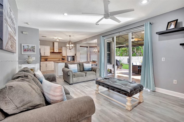 living room featuring a textured ceiling, ceiling fan with notable chandelier, and light wood-type flooring