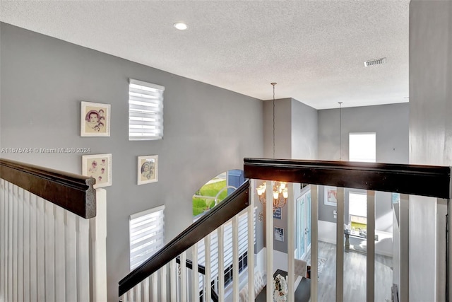 staircase with a healthy amount of sunlight, a textured ceiling, and a chandelier