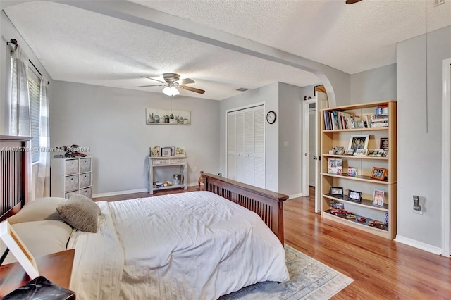 bedroom featuring light hardwood / wood-style flooring, a textured ceiling, a closet, and ceiling fan