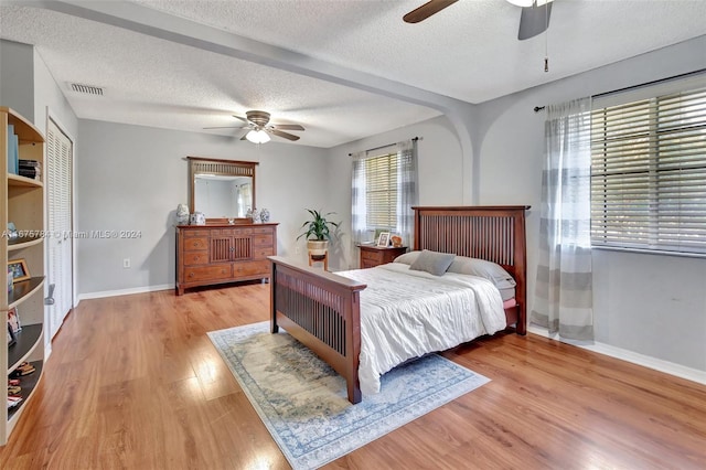 bedroom with light hardwood / wood-style flooring, a textured ceiling, and ceiling fan