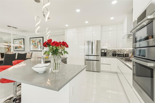 kitchen with white cabinetry, stainless steel appliances, hanging light fixtures, and a breakfast bar area