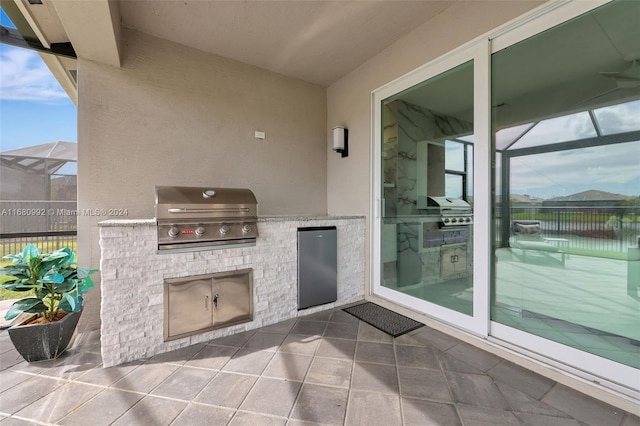 view of patio featuring glass enclosure, grilling area, and an outdoor kitchen