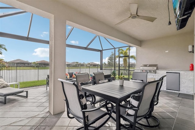 view of patio / terrace with a lanai, grilling area, exterior kitchen, ceiling fan, and a water view