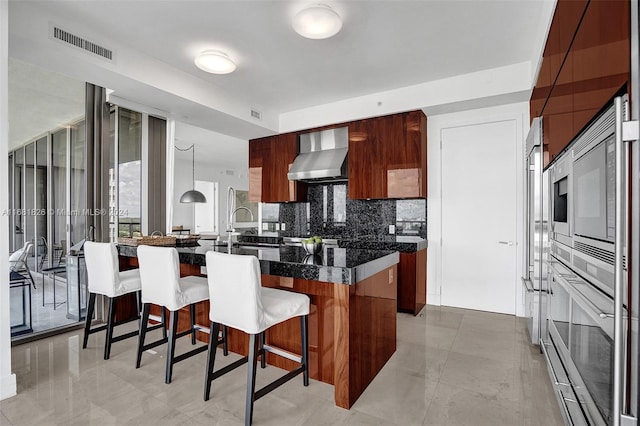 kitchen with a breakfast bar, wall chimney range hood, decorative light fixtures, and tasteful backsplash