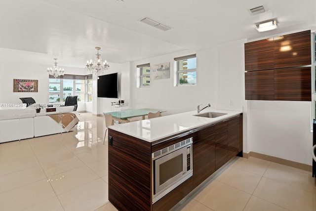 kitchen with hanging light fixtures, stainless steel microwave, a chandelier, light tile patterned flooring, and sink