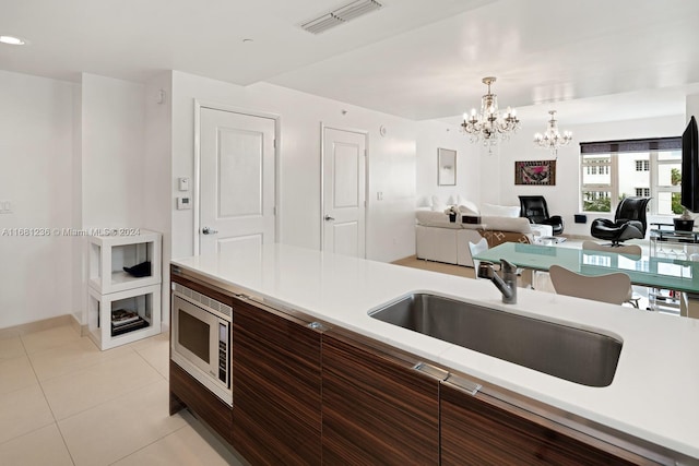 kitchen with sink, stainless steel microwave, pendant lighting, light tile patterned floors, and an inviting chandelier