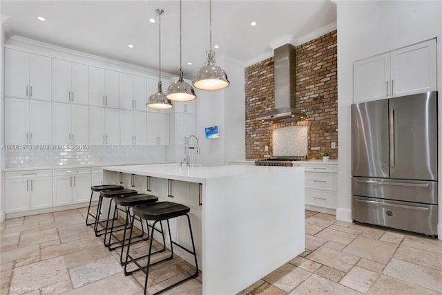 kitchen with wall chimney range hood, decorative backsplash, white cabinets, appliances with stainless steel finishes, and pendant lighting