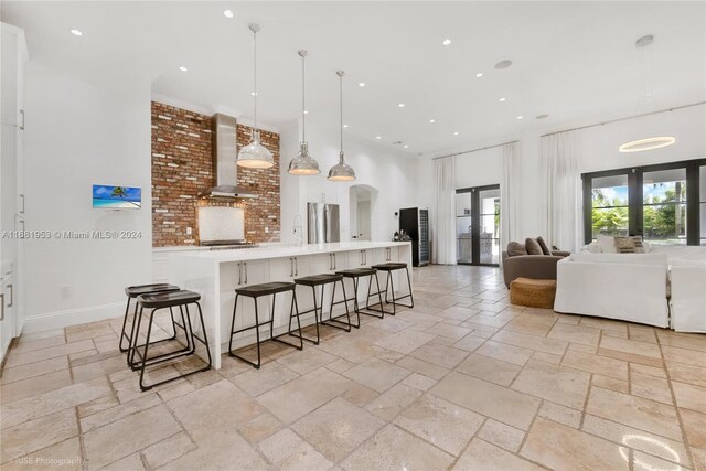 kitchen featuring french doors, wall chimney range hood, white cabinetry, and pendant lighting