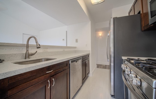 kitchen with light wood-type flooring, stainless steel appliances, dark brown cabinetry, sink, and light stone counters