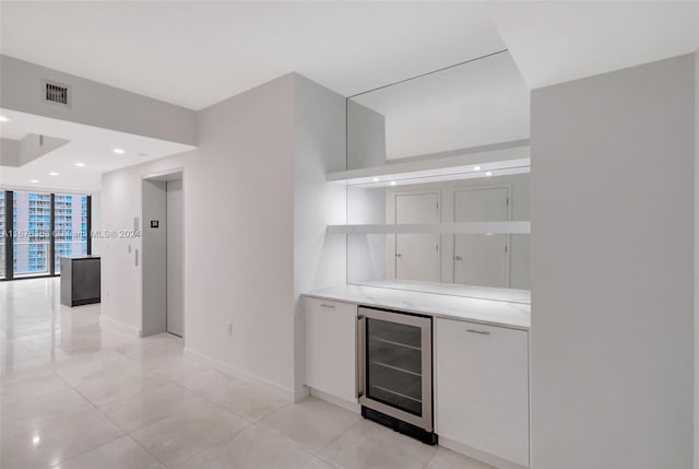 bar with wine cooler, white cabinets, light tile patterned floors, floor to ceiling windows, and elevator