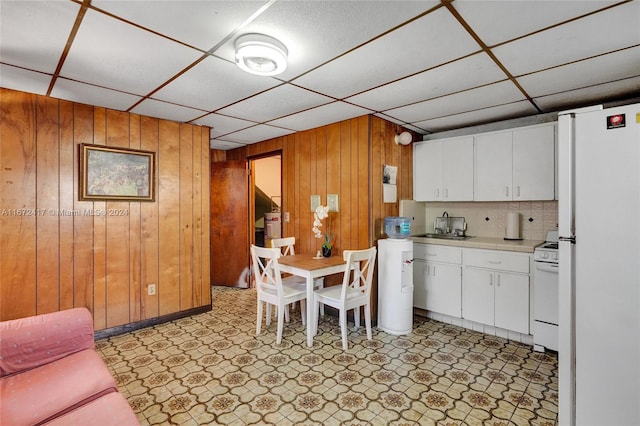 kitchen featuring white appliances, wood walls, sink, backsplash, and white cabinets