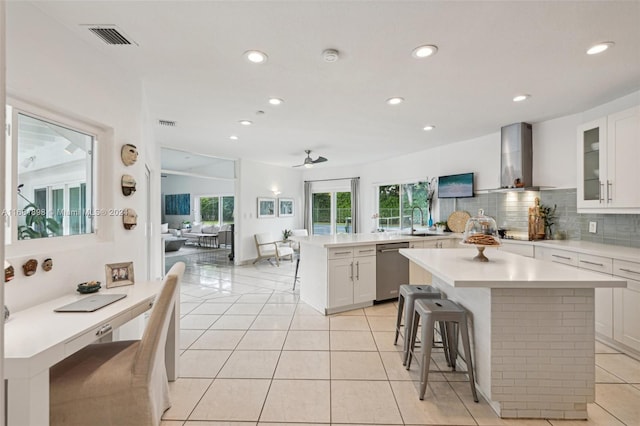 kitchen featuring wall chimney range hood, a breakfast bar, a kitchen island, and white cabinets