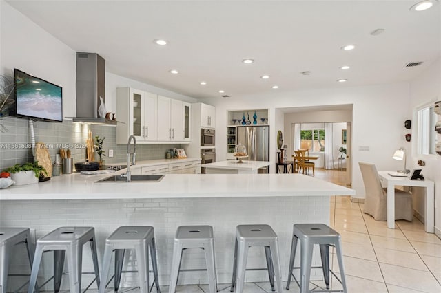 kitchen with wall chimney range hood, a kitchen bar, kitchen peninsula, white cabinetry, and stainless steel refrigerator