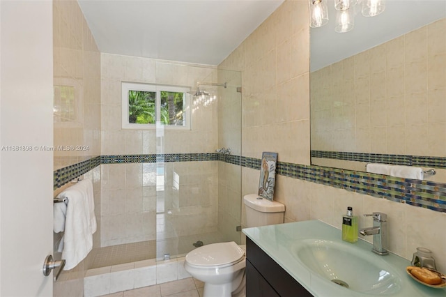 bathroom with tile patterned floors, toilet, tile walls, vanity, and a tile shower