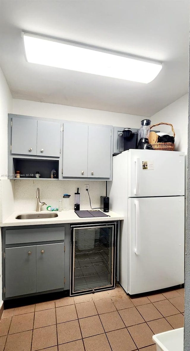 kitchen with gray cabinets, beverage cooler, sink, and white refrigerator