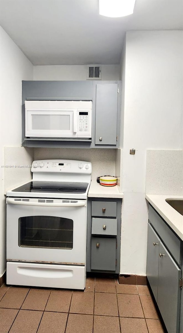 kitchen with tile patterned flooring, white appliances, and gray cabinetry