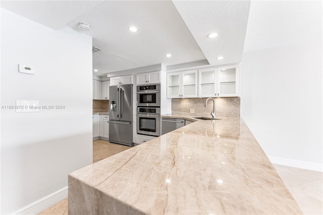 kitchen with backsplash, sink, light stone countertops, white cabinets, and appliances with stainless steel finishes