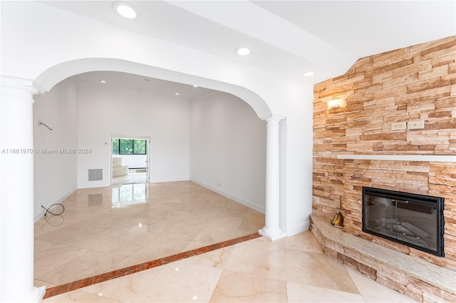 unfurnished living room featuring a stone fireplace, crown molding, and decorative columns