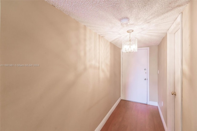 corridor featuring a textured ceiling, hardwood / wood-style flooring, and an inviting chandelier