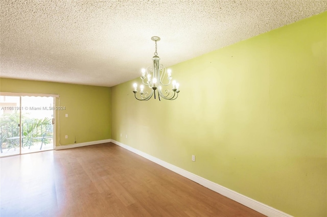 empty room featuring wood-type flooring, a textured ceiling, and a chandelier