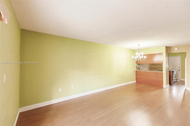 spare room with a notable chandelier, a textured ceiling, and light wood-type flooring